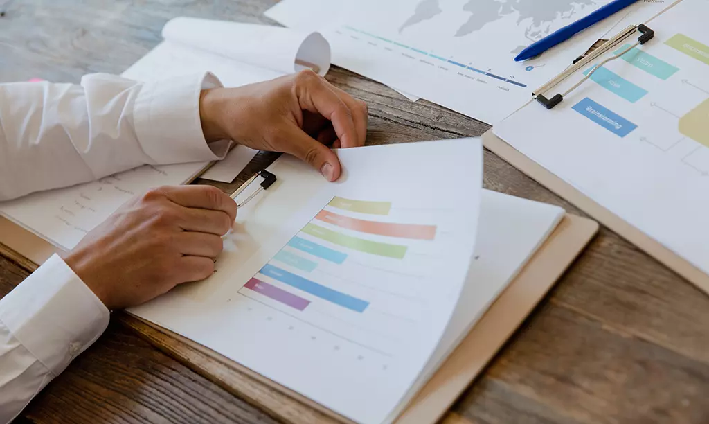 Pessoa analisando relatórios financeiros e gráficos sobre uma mesa, com documentos e planilhas utilizados para planejamento financeiro.