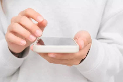 Close-up de mãos utilizando um smartphone com tela apagada, em ambiente claro e minimalista.