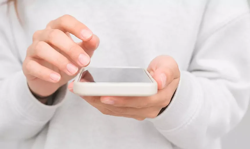 Close-up de mãos utilizando um smartphone com tela apagada, em ambiente claro e minimalista.