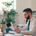 Homem analisando documentos e contas em um escritório doméstico.