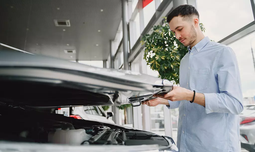 Homem inspecionando o compartimento do motor de um carro usado em uma concessionária antes da compra.