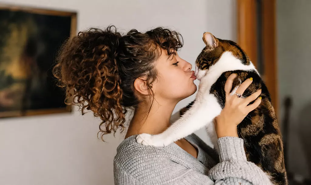 Mulher segurando e beijando um gato dentro de casa, representando a relação entre tutores e pets na Irlanda.